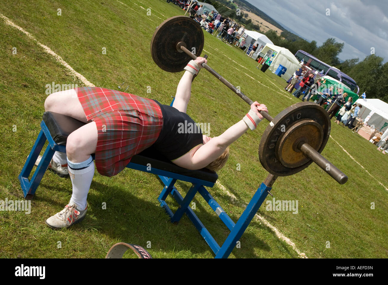Corpo di donna builder indossa kilt. Donna forte sollevamento pesi, onorevoli sollevamento banco premere Barbell a Falkirk Giochi delle Highland, Scotland Regno Unito Foto Stock