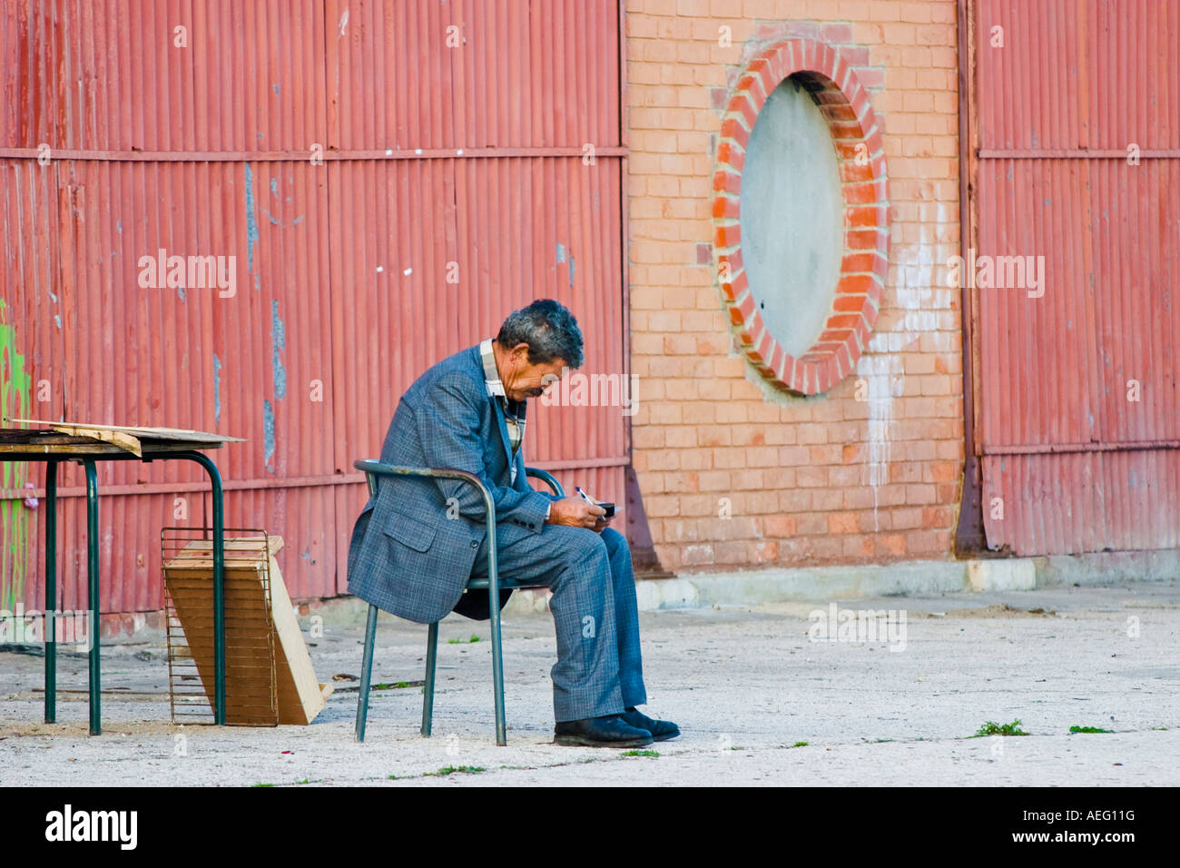 Il vecchio uomo seduto da solo all'esterno rivolto verso il basso tenendo la penna e carta cercando triste Foto Stock