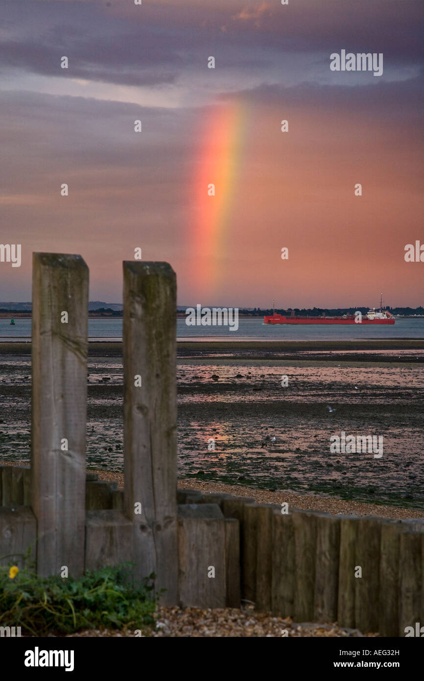 Rainbow parziale sulla spiaggia Calshot vicino a Southampton acqua con piccole navi cisterna Foto Stock