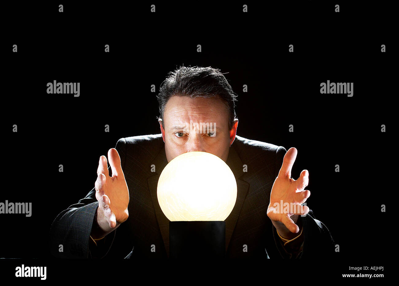 Un uomo d'affari contro uno sfondo nero guardando intensamente in una illuminata internamente sfera di cristallo Foto Stock