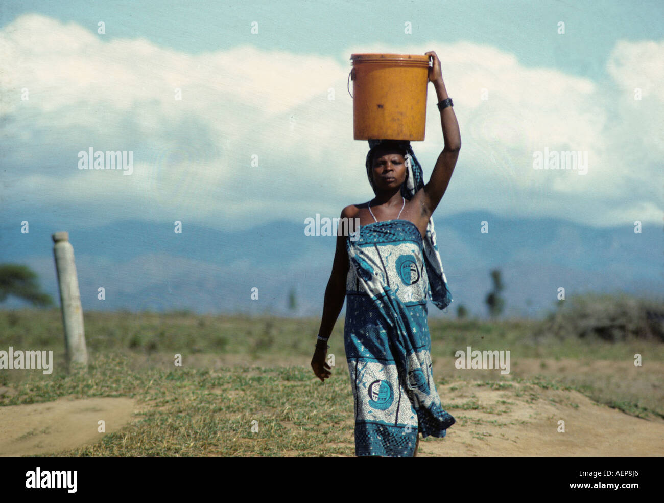 AF Tanzania: una donna porta un secchio grande sul suo capo. Foto Stock