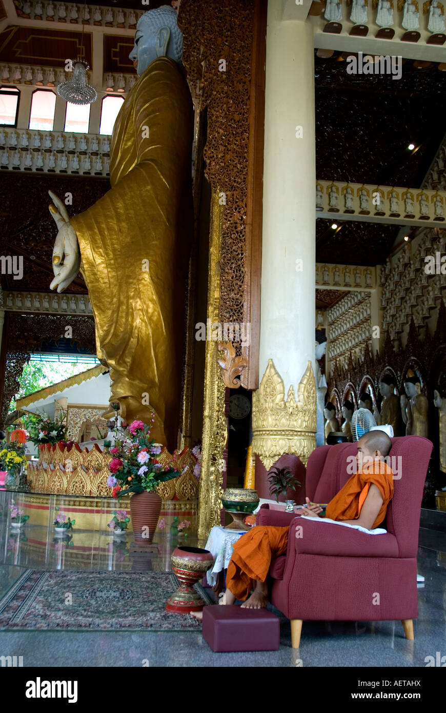 Un monaco appoggiato accanto a una gigantesca statua di Buddha Foto Stock
