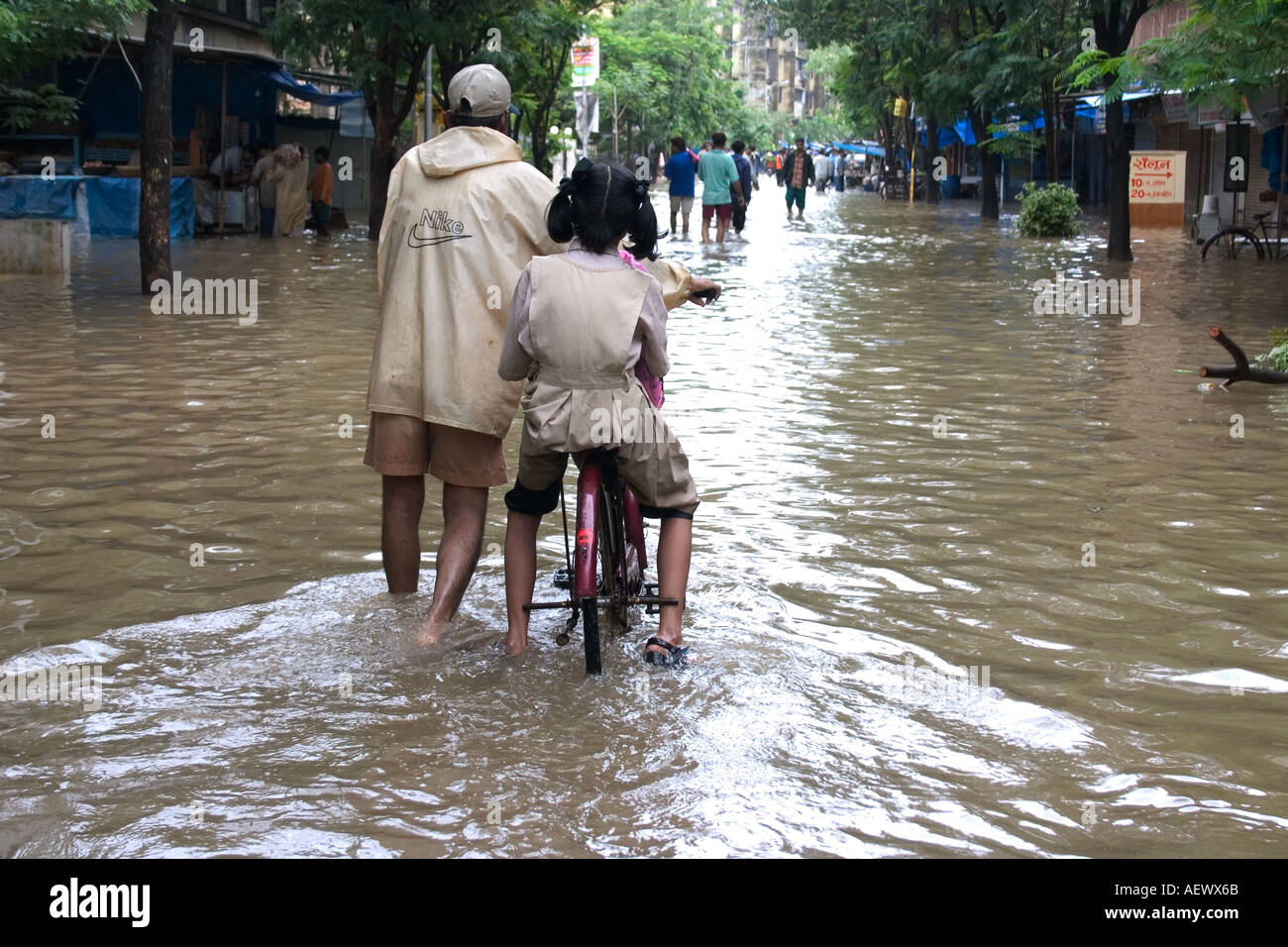 Uomo con bambini in bicicletta a piedi in strada allagata dopo monsone pioggia, Bombay, Mumbai, Maharashtra, India, Asia Foto Stock