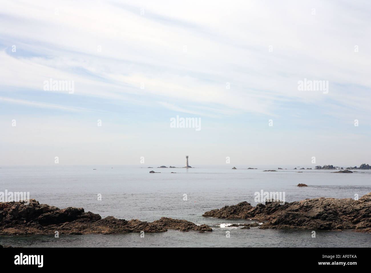 Mare calmo al di là del promontorio roccioso e del faro sulla costa di Guernsey nelle isole del canale U K Foto Stock