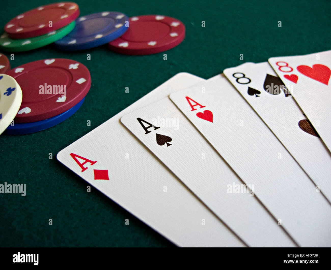 Mano di Poker, Full House, Aces su Ottavi con le carte ventaglio su un feltro verde il piano portapaziente che contiene anche un paio di poker chips Foto Stock