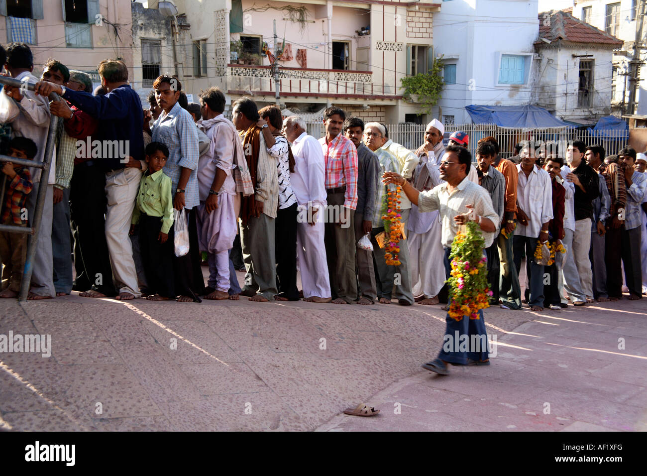 Indiano maschio che offre la vendita di ghirlande a grande coda di adoratori maschili che accodano fuori del Tempio di Dwarkadhish, Dwarka, Gujarat, India Foto Stock