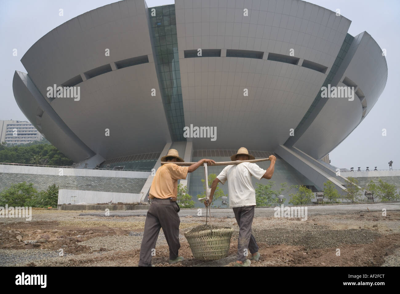 Lavoratori cestello di trasporto con tracolla in pole davanti a stadio moderno Fengjie Cina Sichuan Foto Stock