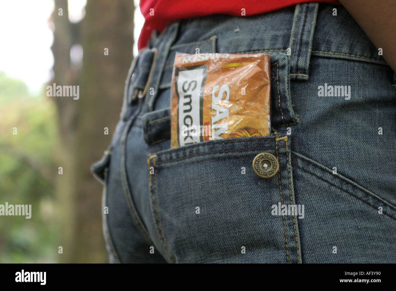 Arrotolare il tabacco busta nella tasca posteriore dei jeans indossato da donna; forse un segnale per i trafficanti di droga Foto Stock