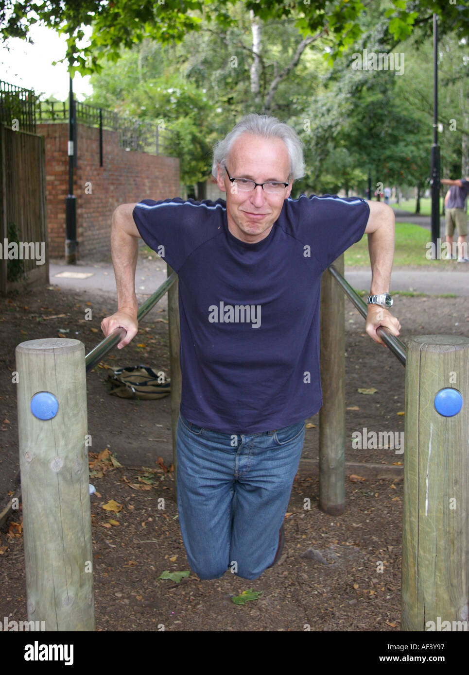 Grigio uomo dai capelli degli anni quaranta lottando esercitando sulle barre parallele in posizione di parcheggio Foto Stock