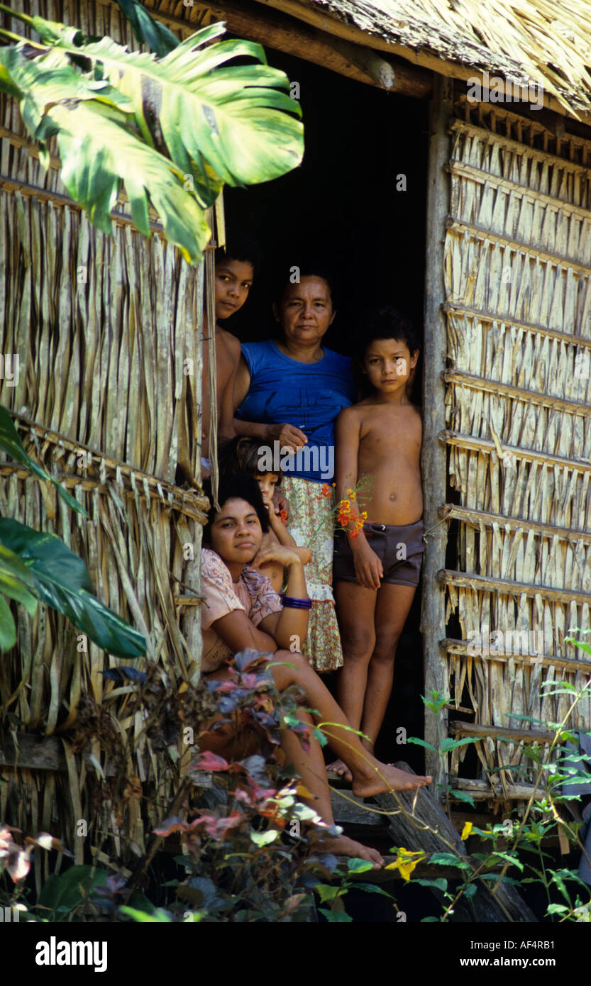 La madre ed i suoi tre bambini in posa per ritratto nella porta della loro foresta pluviale di paglia di casa nella regione amazzonica del Brasile Foto Stock