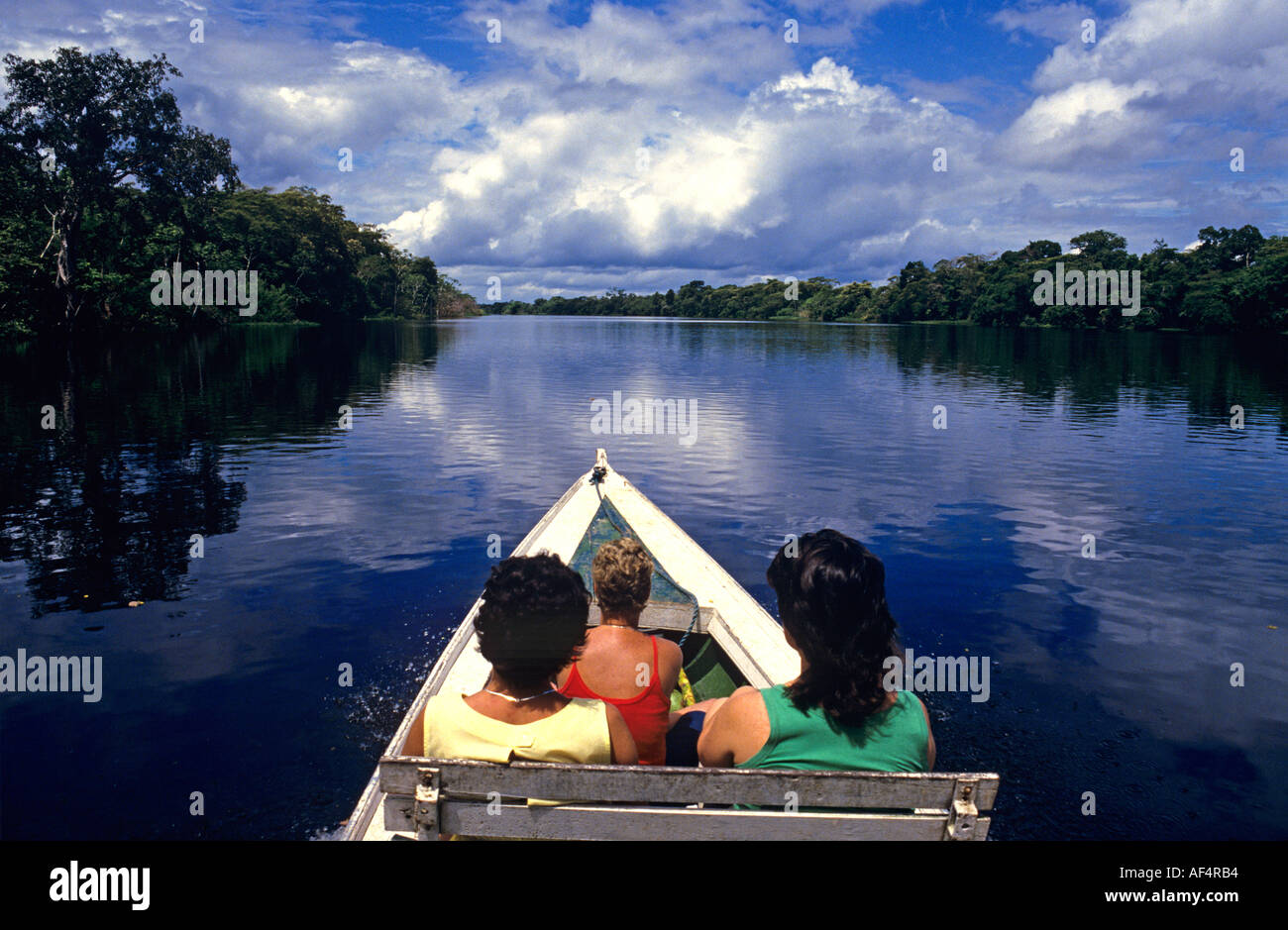 Due lady visitatori in locale in stile piroga canoa sulle acque di un fiume in uno scenario della foresta pluviale nella regione amazzonica del Brasile Foto Stock