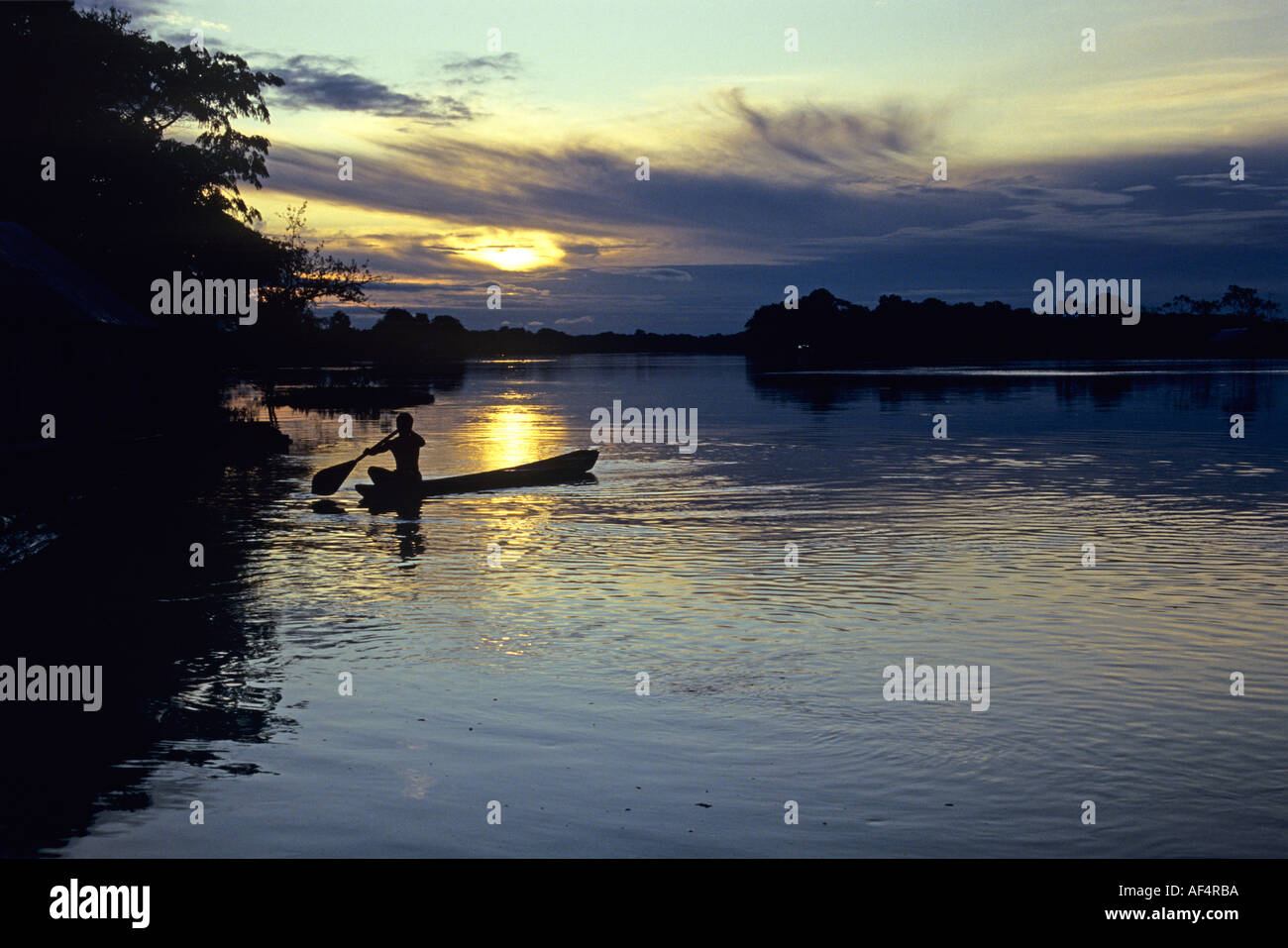 Uomo locale pagaie canoa contro il tramonto sul fiume e profila uno scenario della foresta pluviale nella regione amazzonica del Brasile Foto Stock
