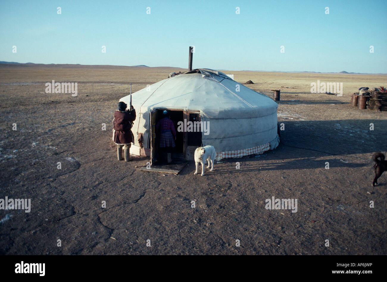 MONGOLIA persone Ger o yurt in winter camp con cani legato al di fuori e pastore nomade in piedi accanto a ingresso e terreno pianeggiante Foto Stock
