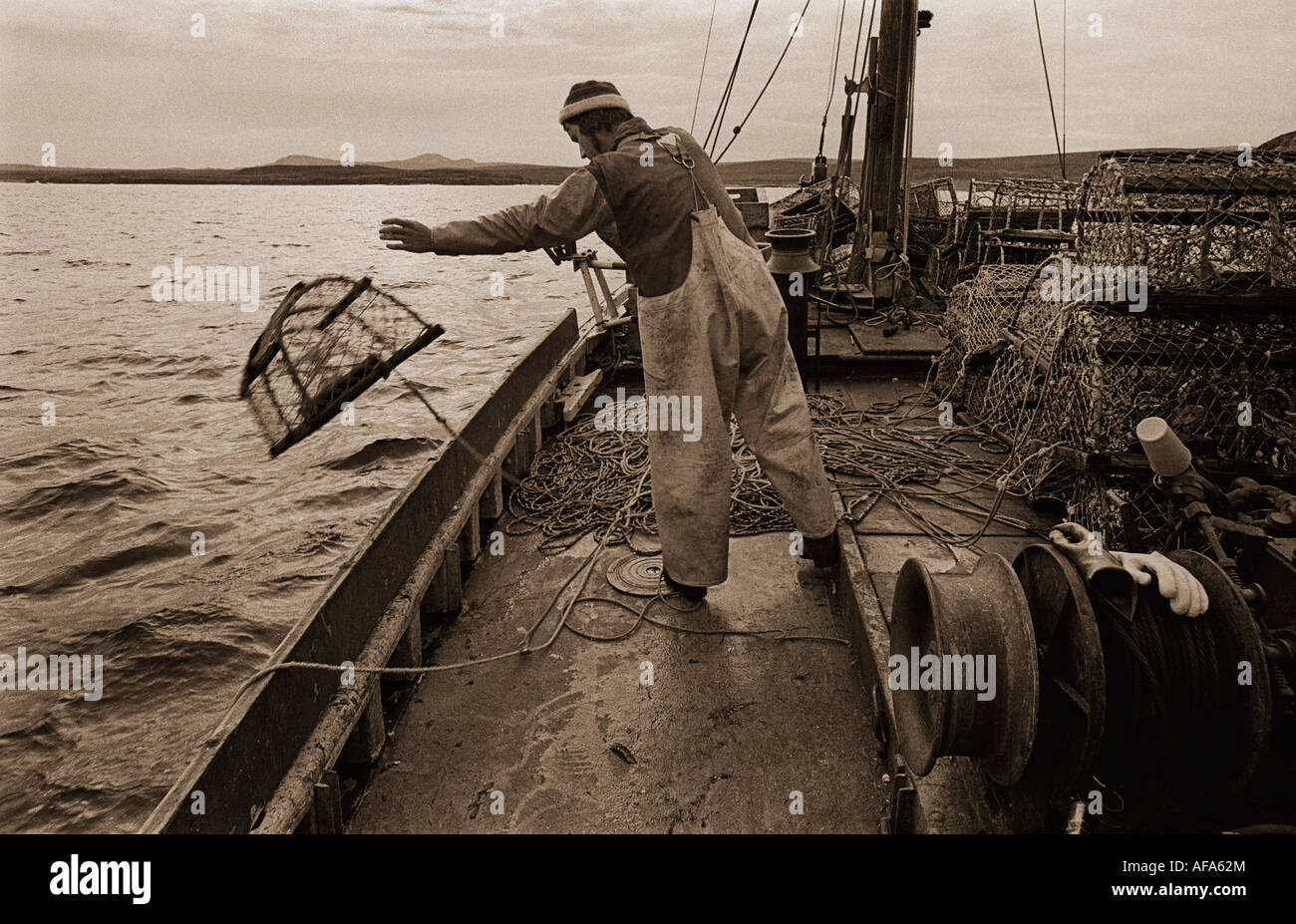 Seppia monocroma oscurata colpo di barca da pesca con crewman gettando lobster-pentole in mare Foto Stock