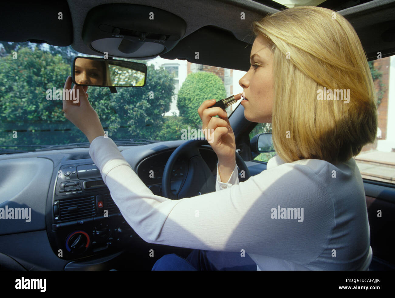 Donna mettendo su make up nella sua auto Foto Stock