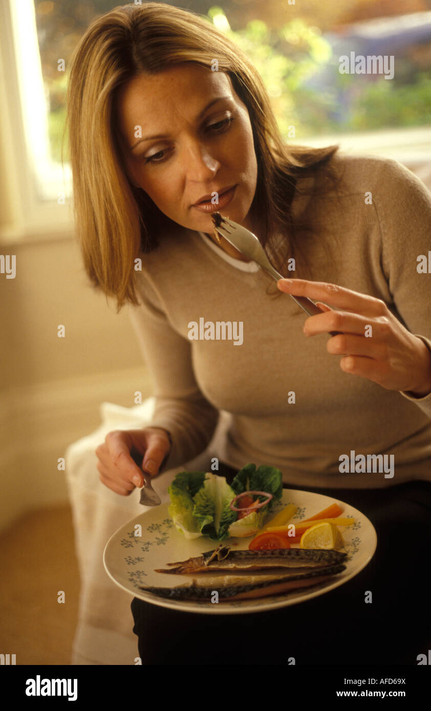 Donna di mangiare pesce oleoso con insalata Foto Stock