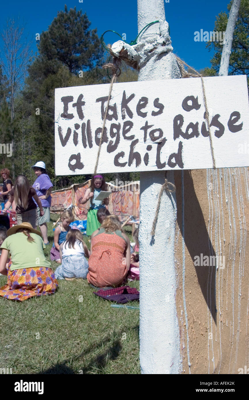 Si prende un villaggio per crescere un bambino scritto sul bordo con un gruppo di bambini e adulti seduti in background Foto Stock