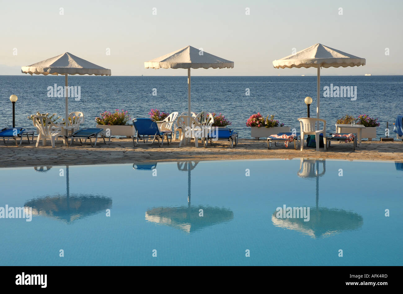 La piscina di mattina presto con acqua bonaccia. Le riflessioni di tre ombrelloni. Sedie e lettini da mare e oltre. Foto Stock