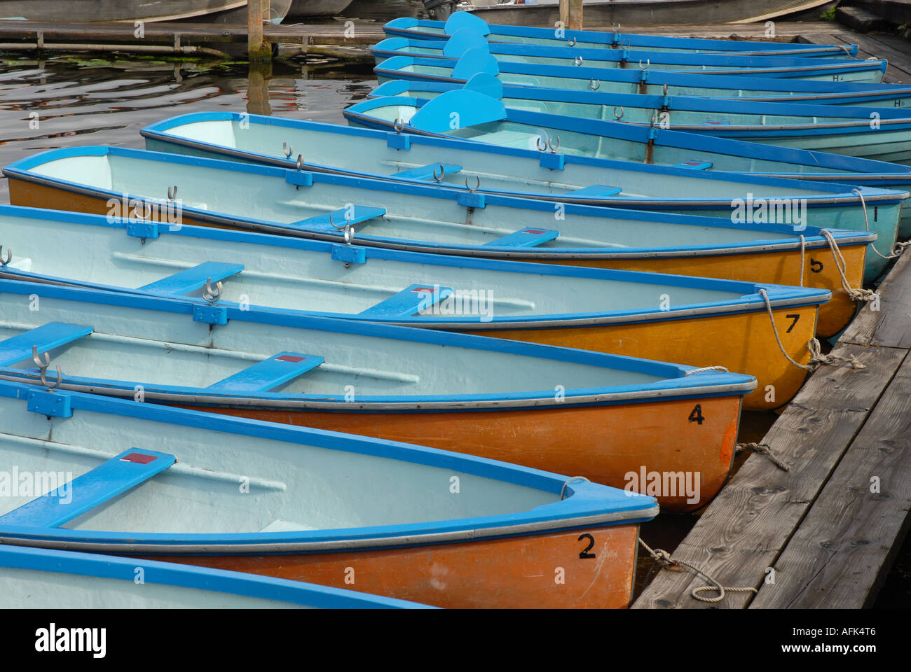 Numerose piccole barche a remi, scafi dipinto in azzurro interno e alcune arancione al di fuori, Ormeggiata al pontile. Foto Stock