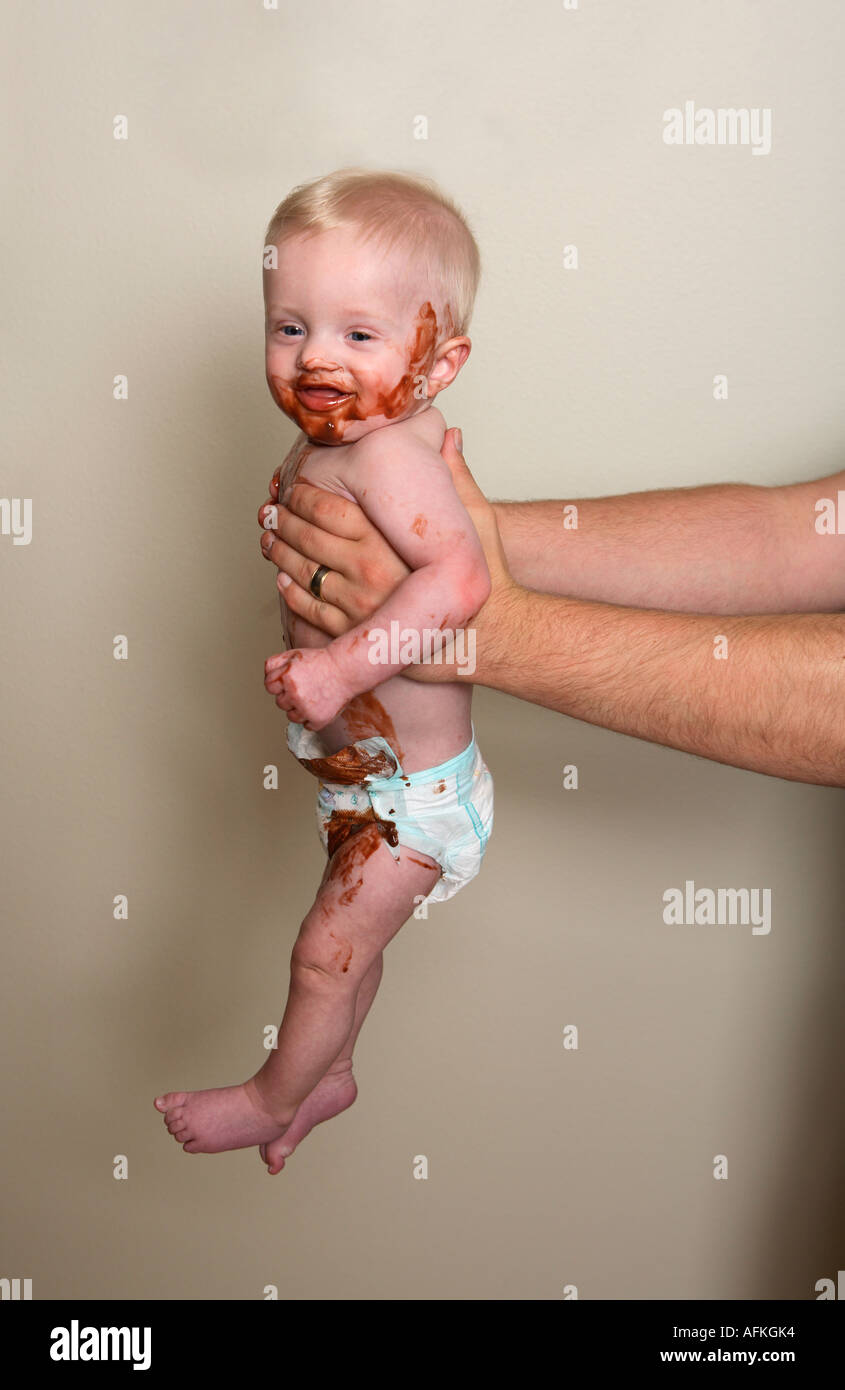 Confuso baby essendo mantenuto a bracci di lunghezza da papà Foto Stock