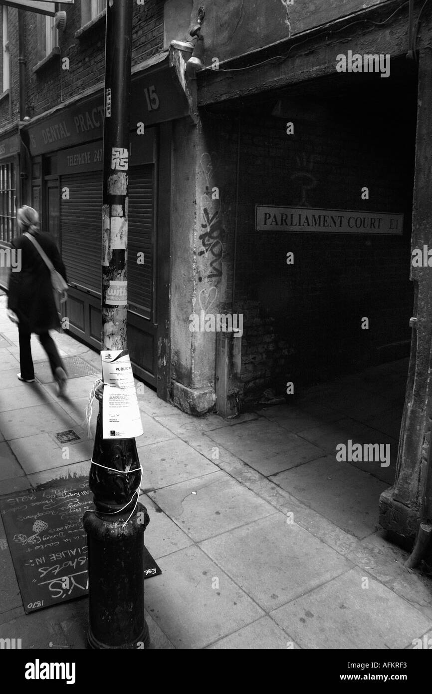 Una donna che cammina verso il basso di uno stretto vicolo in Spitalfields a Londra REGNO UNITO Foto Stock
