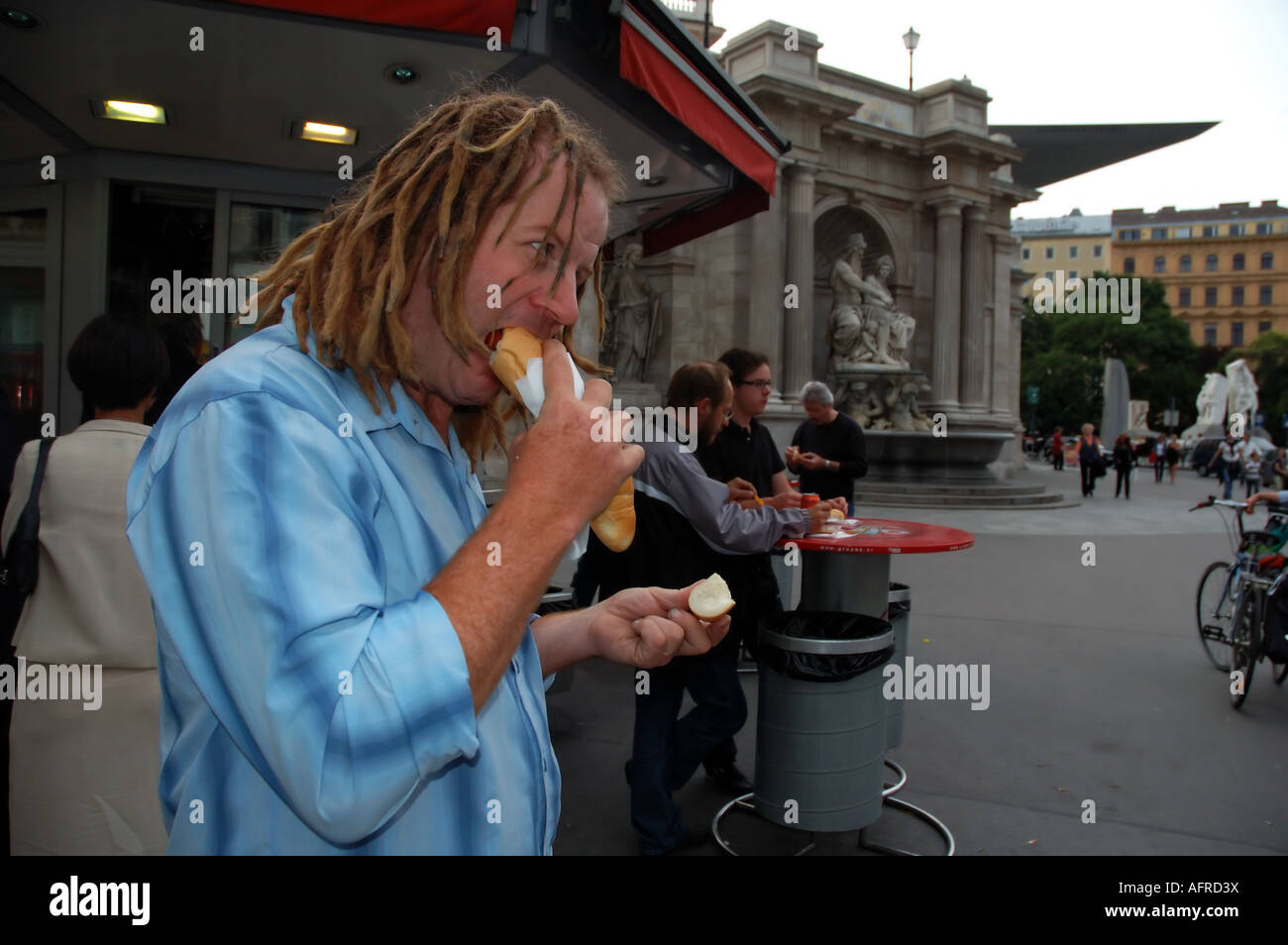 Uomo di mangiare la salsiccia in un panino da una salsiccia wurstelstand stand nel centro di Vienna Austria n. MR Foto Stock