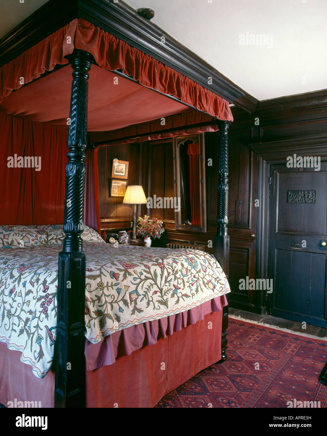Antiquariato in legno intagliato fourposter letto con baldacchino rosso e copriletto crewelwork nel paese camera da letto con pareti rivestite di pannelli Foto Stock