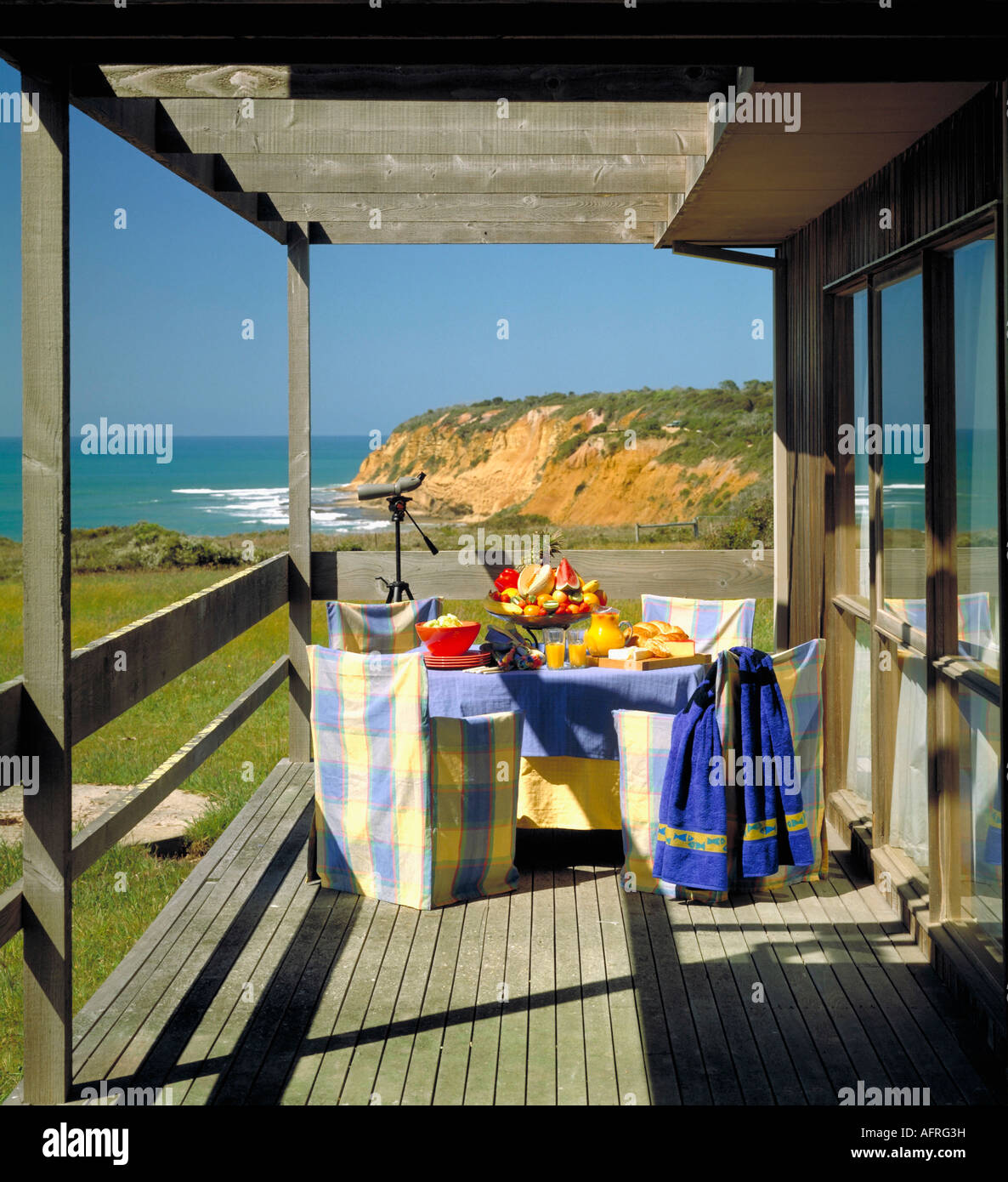 Blu e Giallo controllato sedie e tavolo prevista per il pranzo sulla veranda in legno di una casa tradizionale in Australia con una vista del mare Foto Stock
