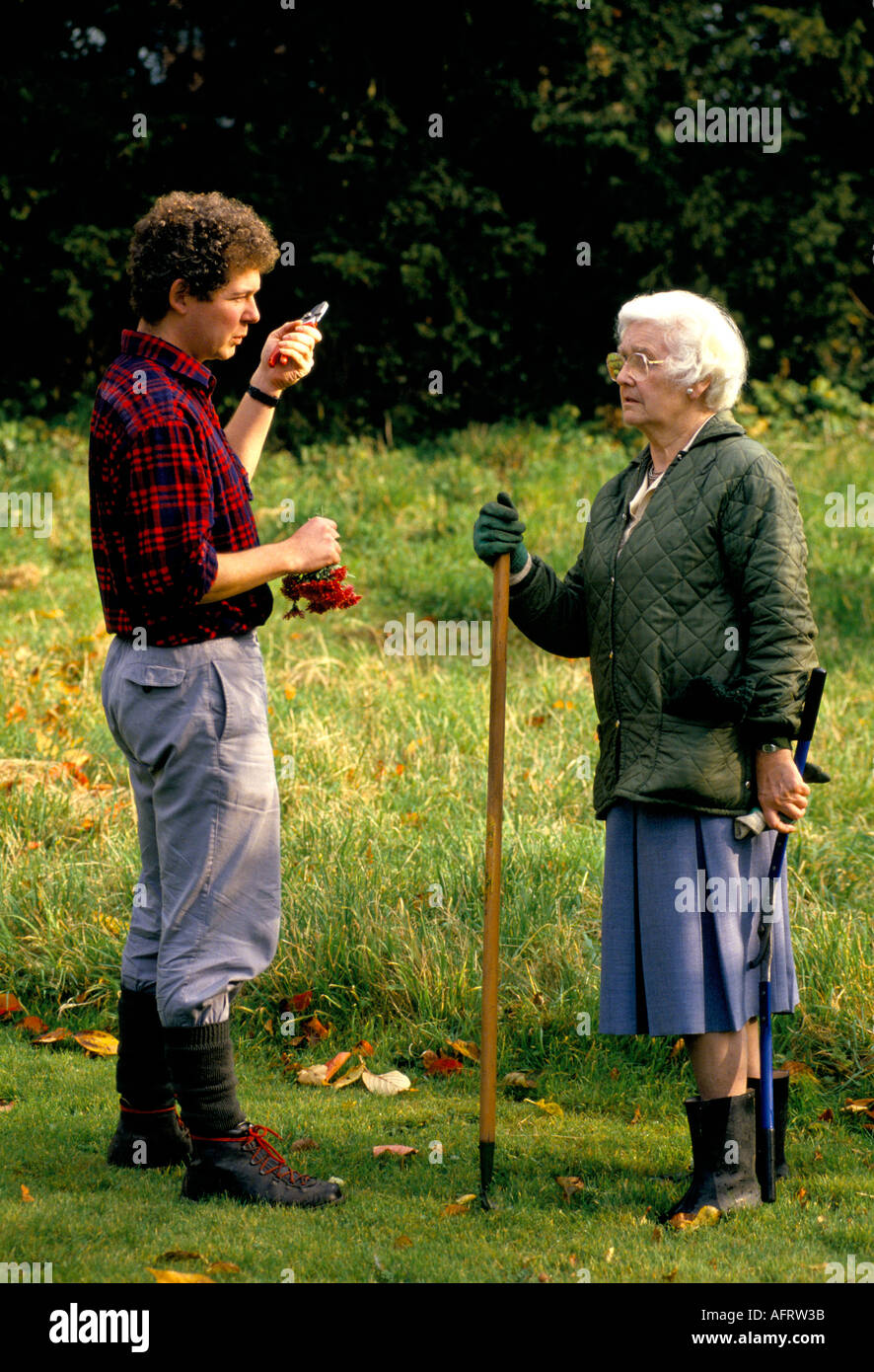Vecchia donna chiacchierando con un giovane uomo nel giardino entrambi giardinaggio GLOUCESTERSHIRE REGNO UNITO HOMER SYKES Foto Stock