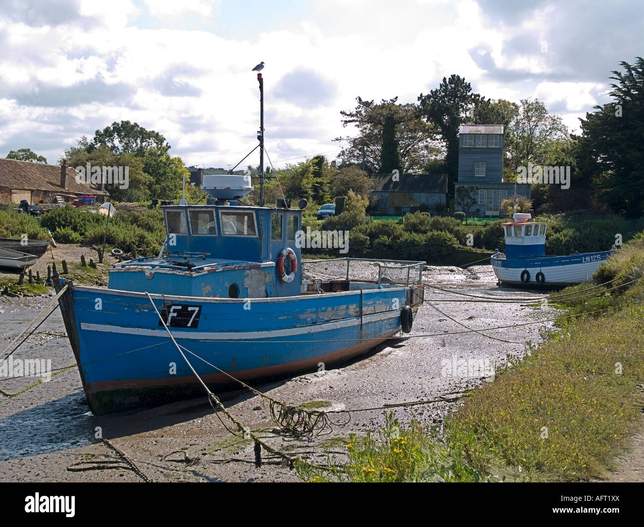 Vecchio Blu barca da pesca appoggia sul fango a bassa marea Brancaster Staithe NORFOLK REGNO UNITO Foto Stock
