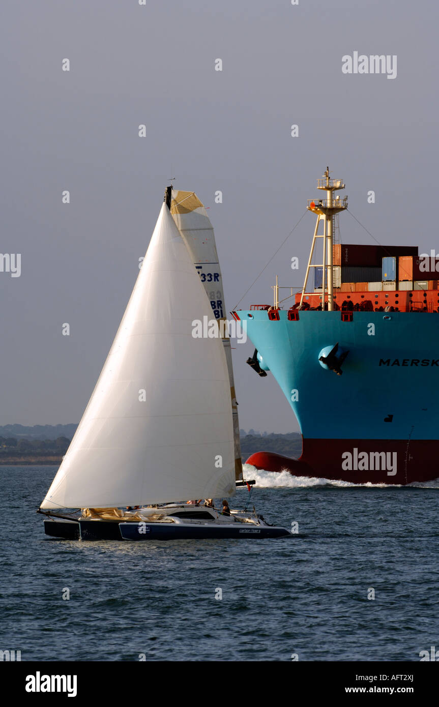 Uno yacht a vela sotto la prua di una grande nave portacontainer nel canale di thorn rotte di navigazione nel solent Foto Stock