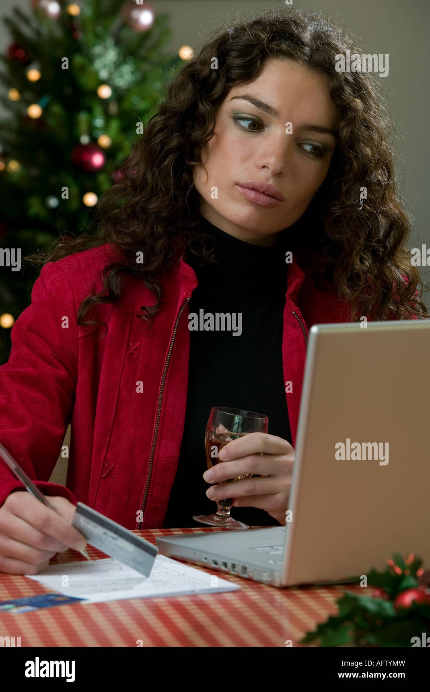 La donna a casa con il computer portatile e carte di credito shopping online con albero di Natale in background Foto Stock