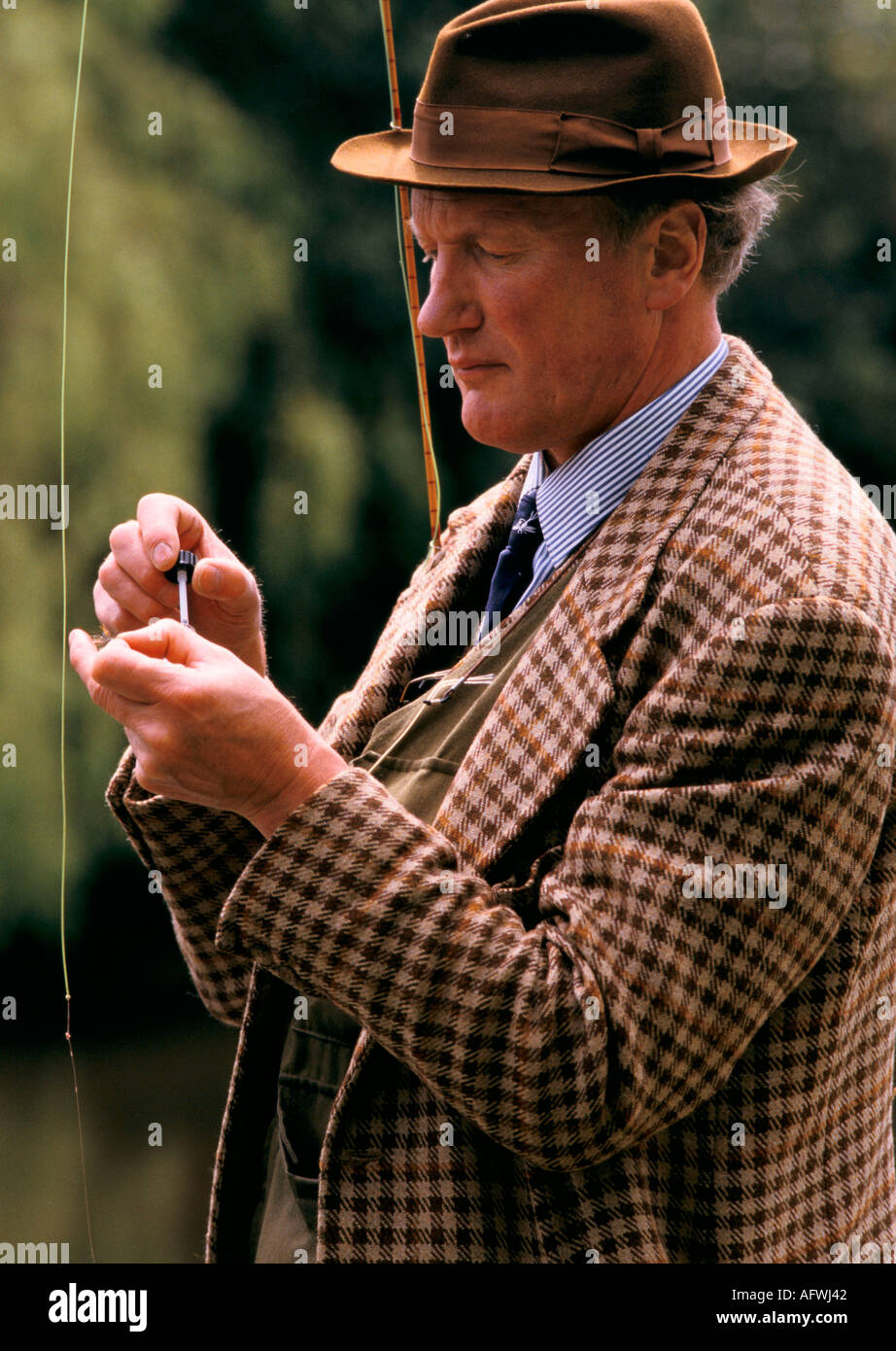 Giacca in tweed UK cappello marrone fedora elegante uomo pesca alla trota che mette una mosca sulla sua linea. John nasce uno sportivo professionista dell'Hampshire degli anni '1980 in Inghilterra Foto Stock