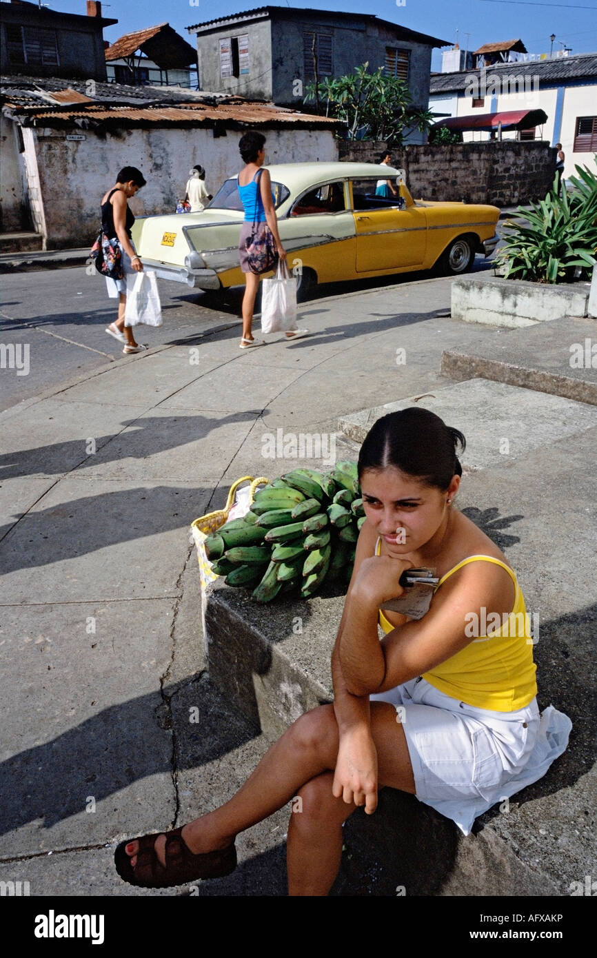 Una giovane donna con un mucchio di banane da cuocere attende per i mezzi di trasporto pubblici Foto Stock