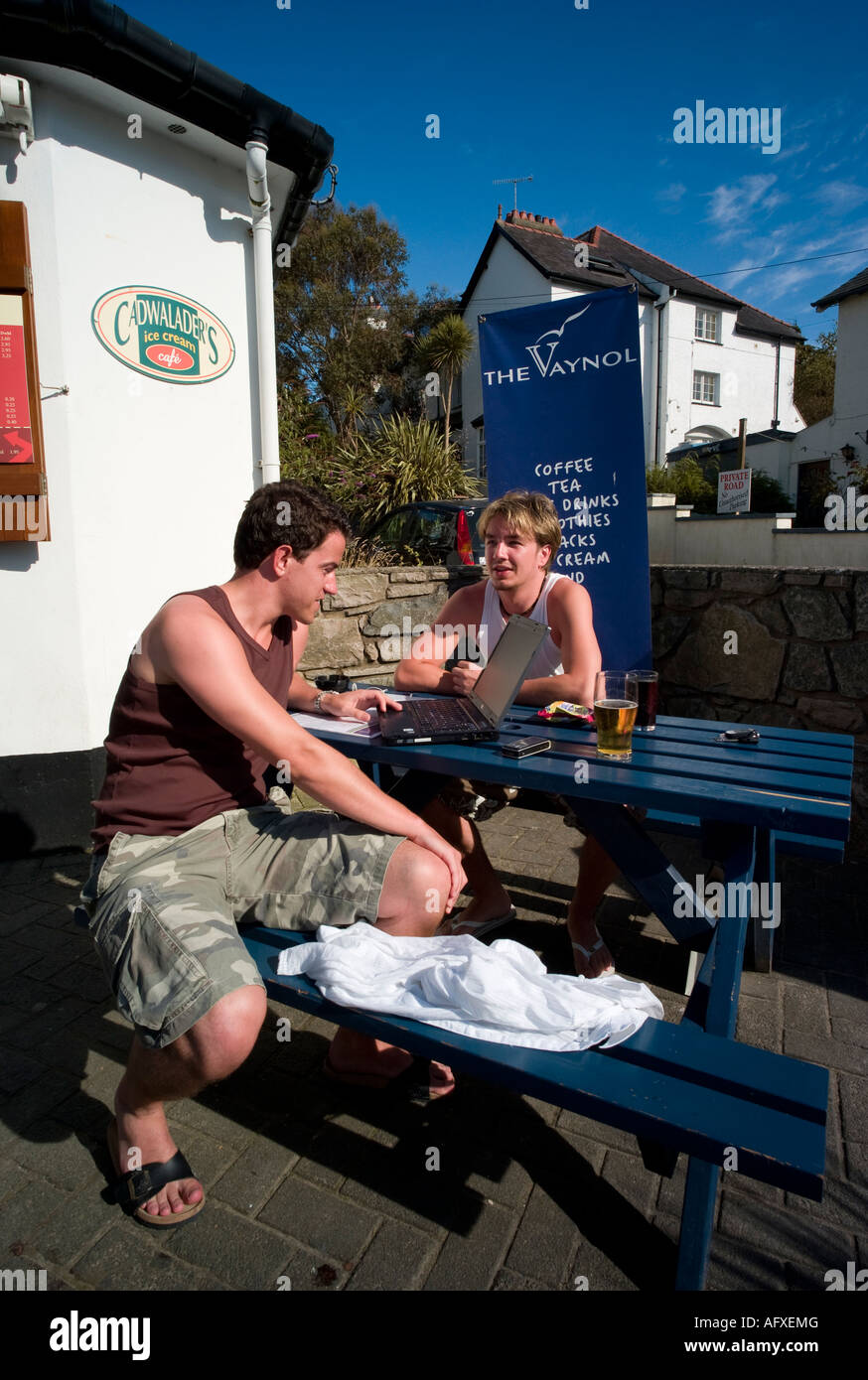 Due cool surfer tipo giovani uomini a parlare e utilizzando computer portatile al di fuori del pub Vaynol Abersoch Gwynedd Galles del nord Foto Stock