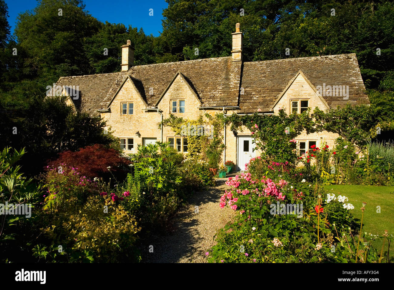 Antico cottage inglese tradizionale cottage gardens con fiori in estate al sole con cielo blu a Bibury Cotswolds UK GB Foto Stock