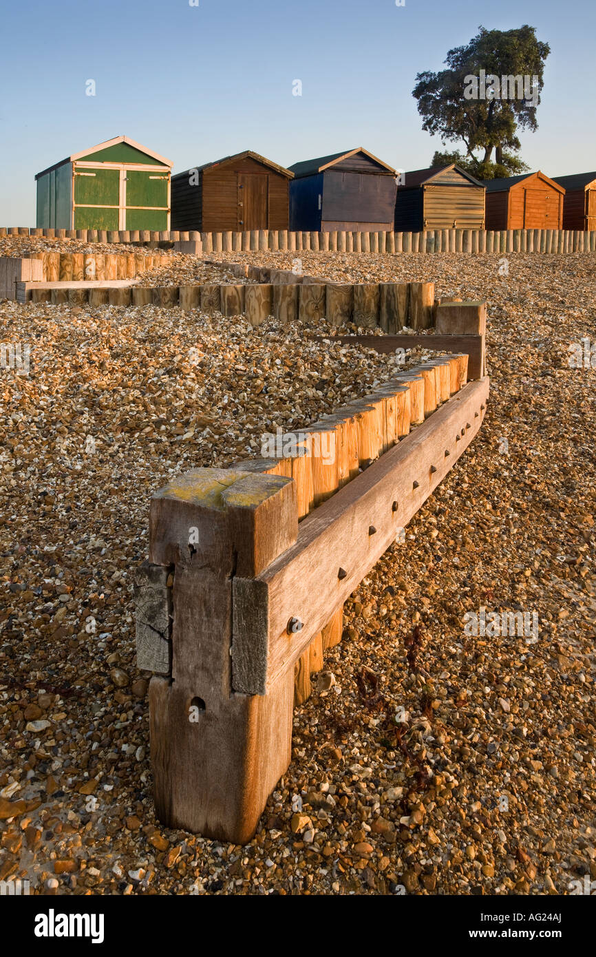 Pennelli in legno per la difesa del mare alla spiaggia di ciottoli a Calshot con capanne in background Foto Stock