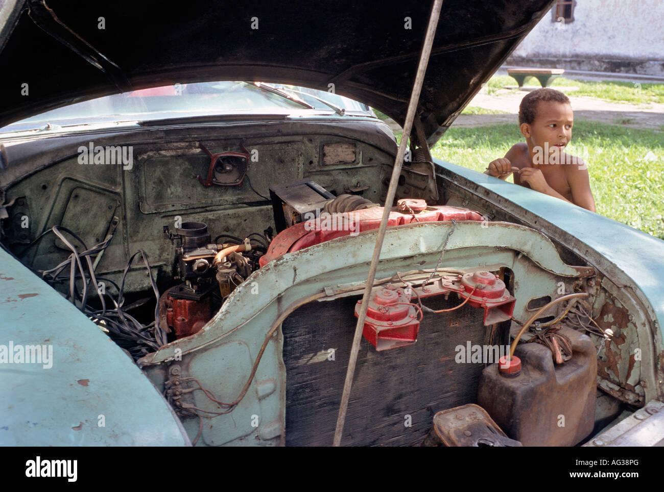 Aprire il cofano di un classico americano auto in Havana Cuba con bambino cubano in background Foto Stock