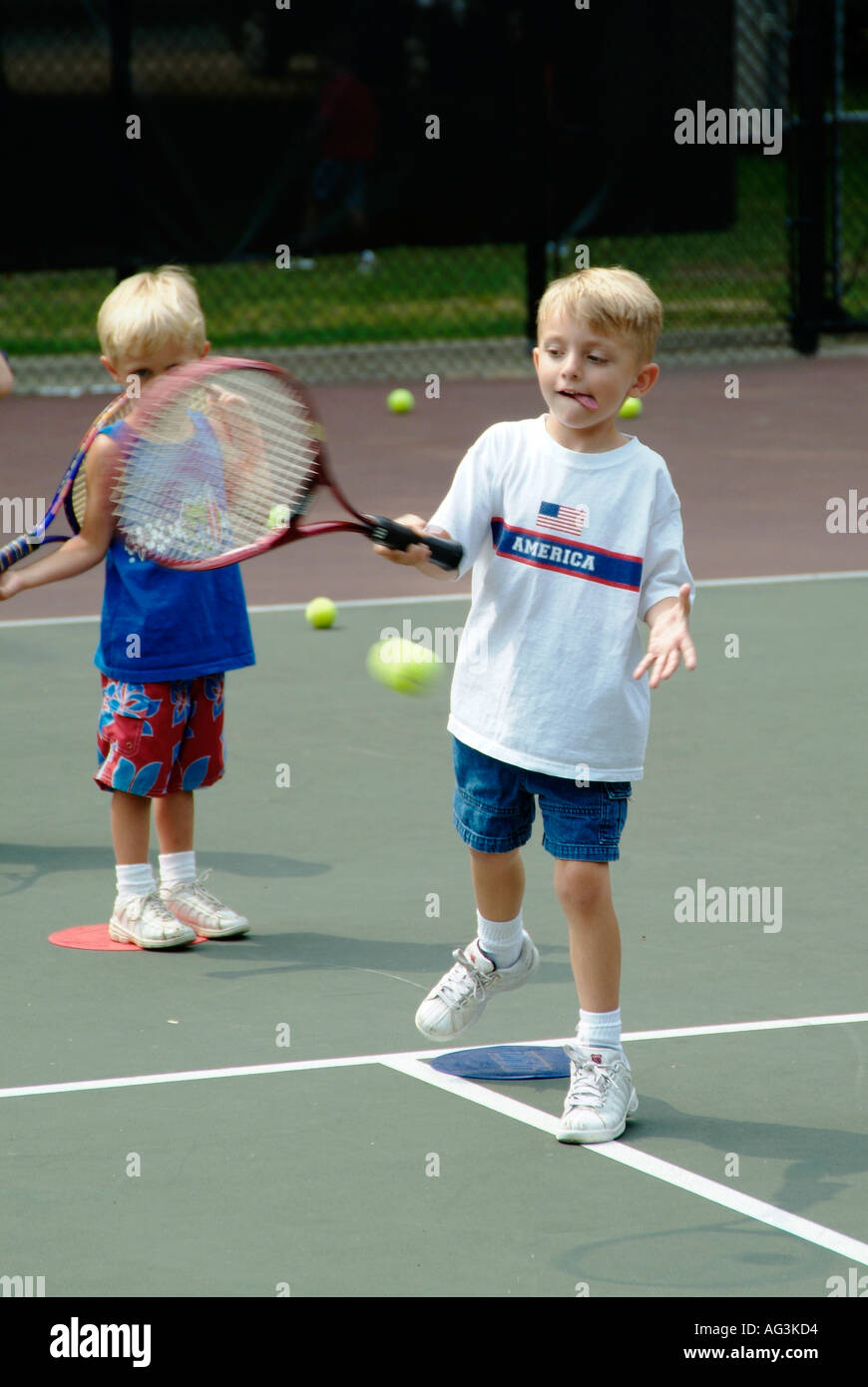 4 e 5 anni i bambini gruppo di prendere lezioni di tennis insegnata da studenti del college a un pubblico campo da tennis Foto Stock