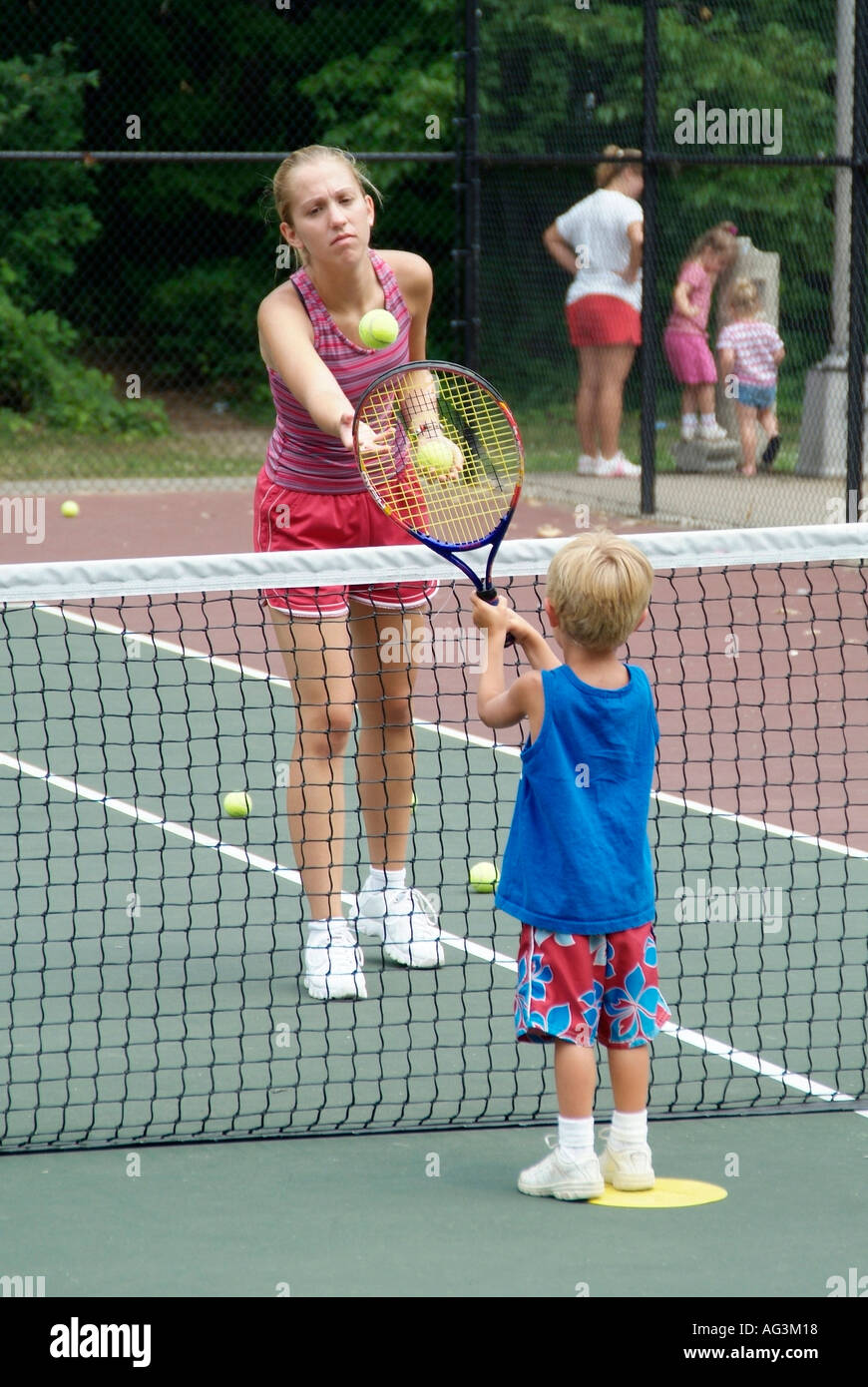 4 e 5 anni i bambini gruppo di prendere lezioni di tennis insegnata da studenti del college a un pubblico campo da tennis Foto Stock