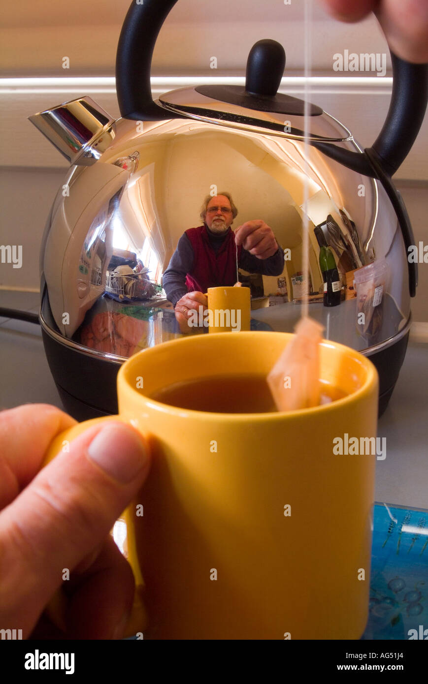 Uomo che prepara una tazza di tè riflesso in un bollitore elettrico in acciaio inossidabile lucido Foto Stock