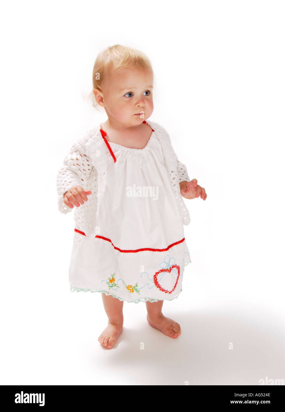 Baby girl in piedi indossando abito bianco con cuore su di esso Foto Stock
