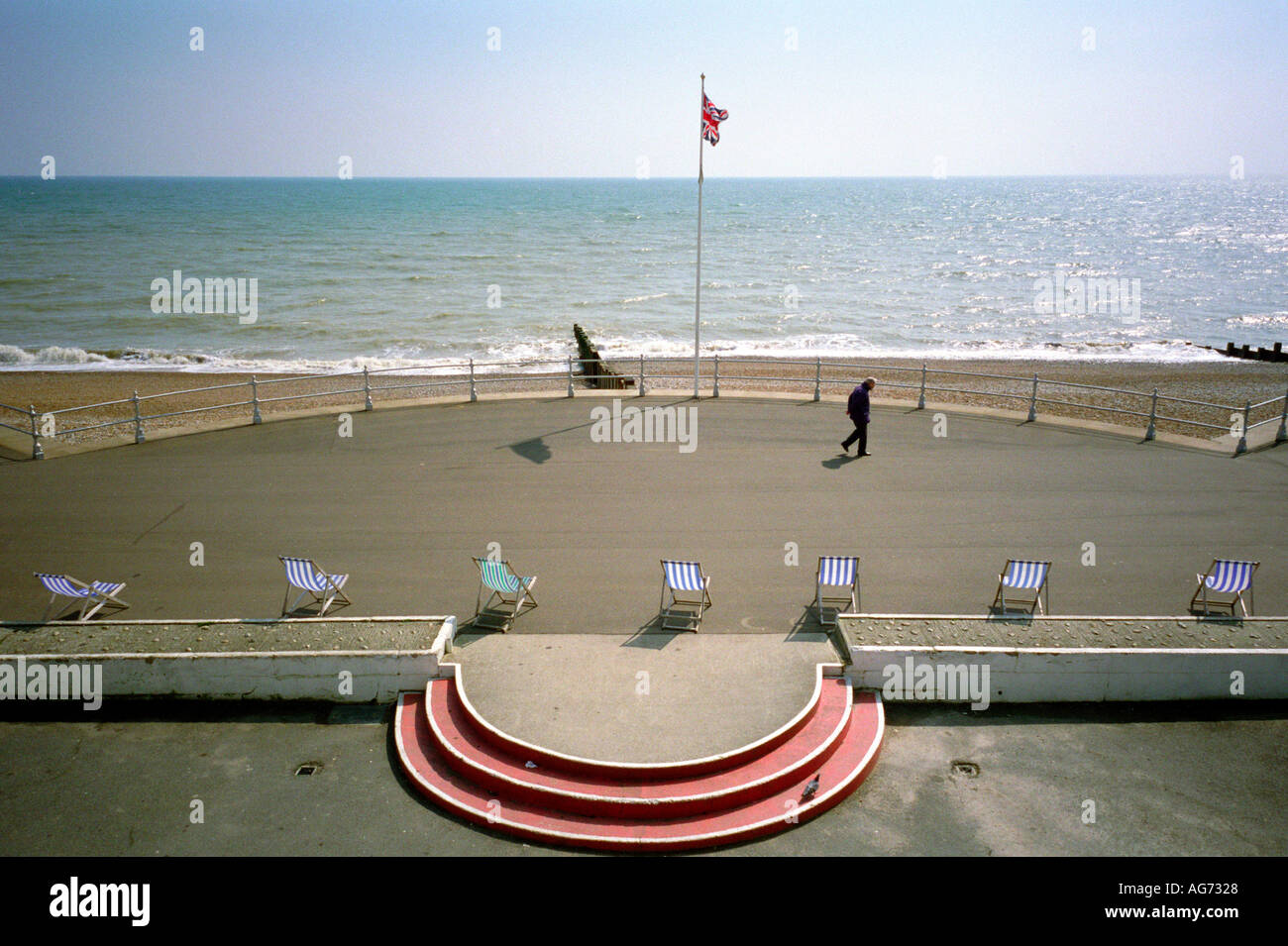 La figura passeggiando lungo la promenade a Bexhill sul mare con sedie a sdraio in primo piano Foto Stock