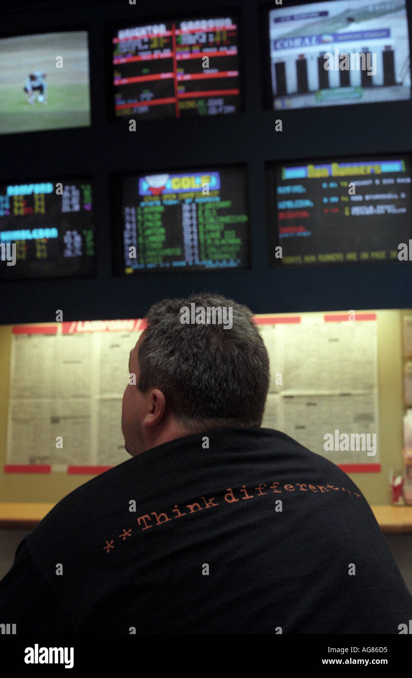 Un punter con un pensare diversi t shirt orologi risultati sportivi presso un negozio di scommesse, Victoria, London, Regno Unito. Foto Stock