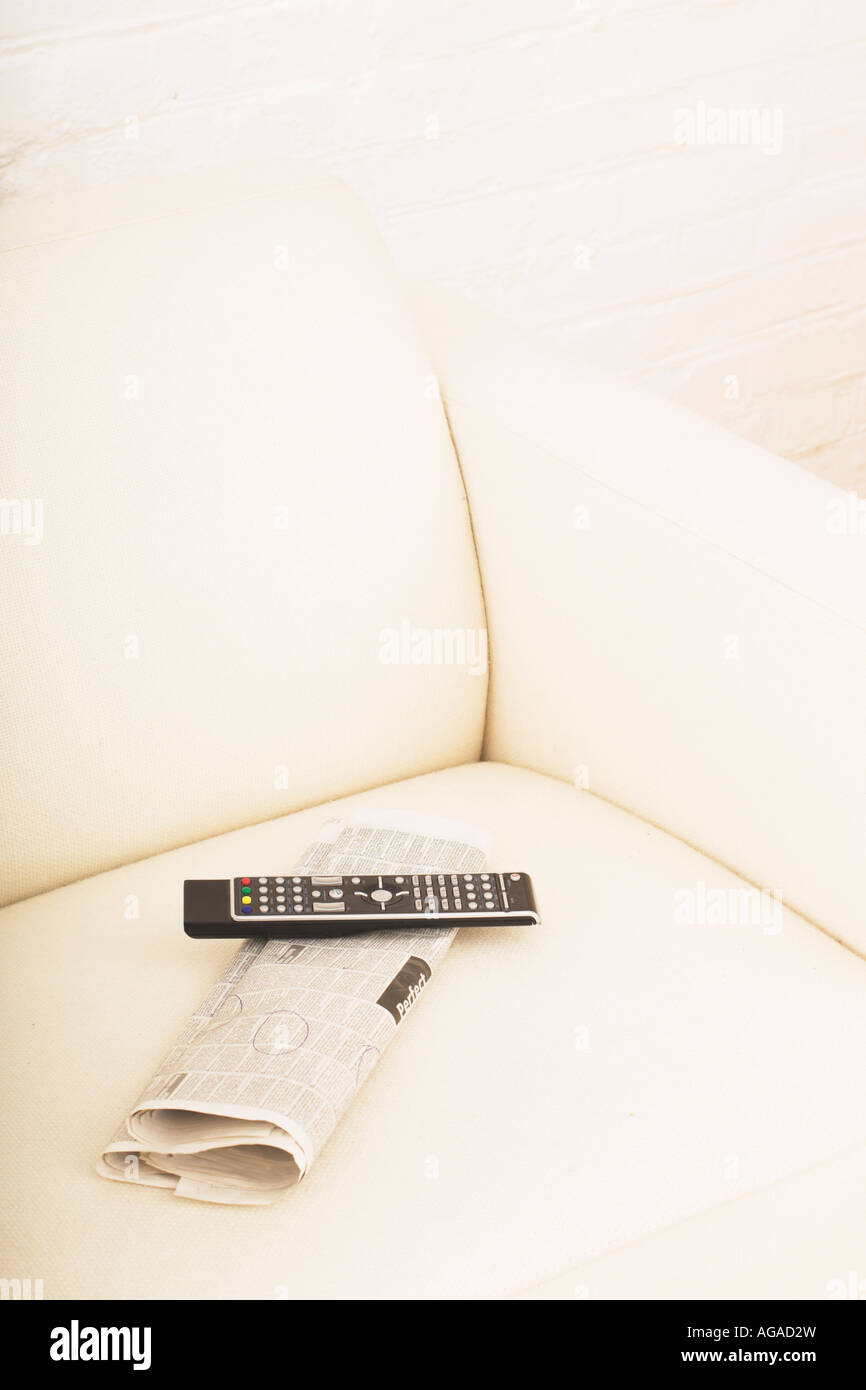 Ancora la vita di giornale e telecomando sulla sedia del braccio Foto Stock