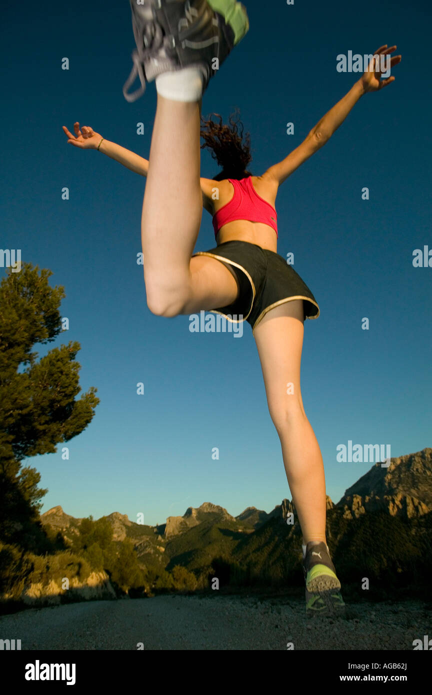 Sentiero femmina runner saltando con sfondo di montagna Foto Stock