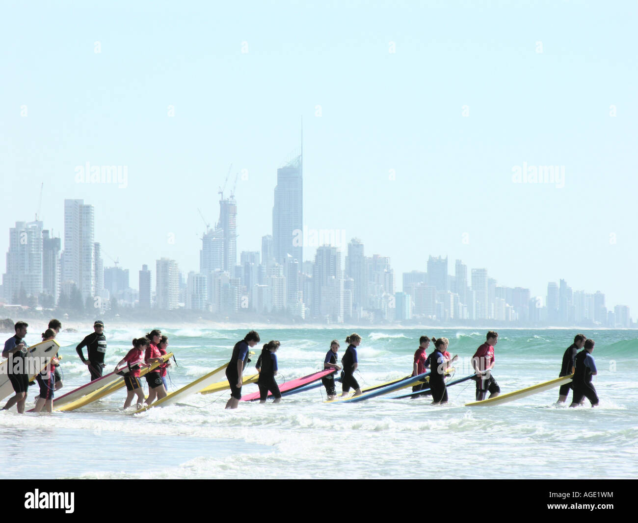 Lezioni di surf surfers passeggiate in mare Goldcoast skyline di distanza Queensland Australia Foto Stock