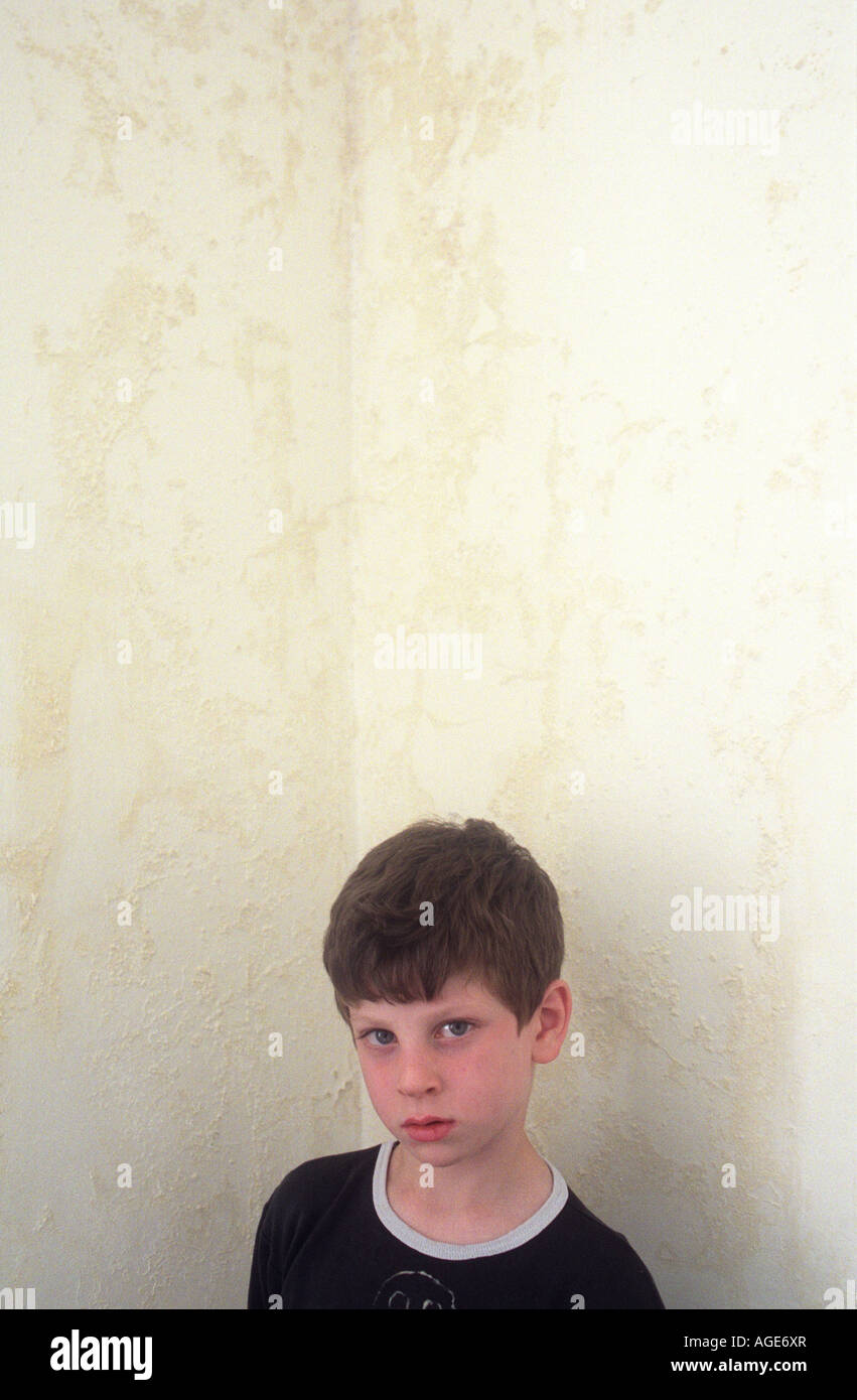 Un ragazzo di 7 anni in piedi di fronte ad un angolo della sua camera da letto danneggiati da umidità. Foto Stock