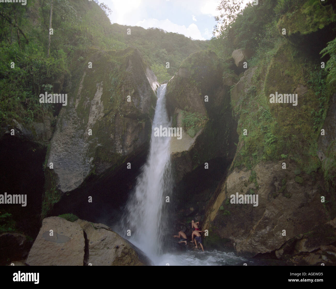 L'acqua cade giù una scenografica scogliera in montagne mentre i ragazzi giocare sotto enormi massi. Foto Stock