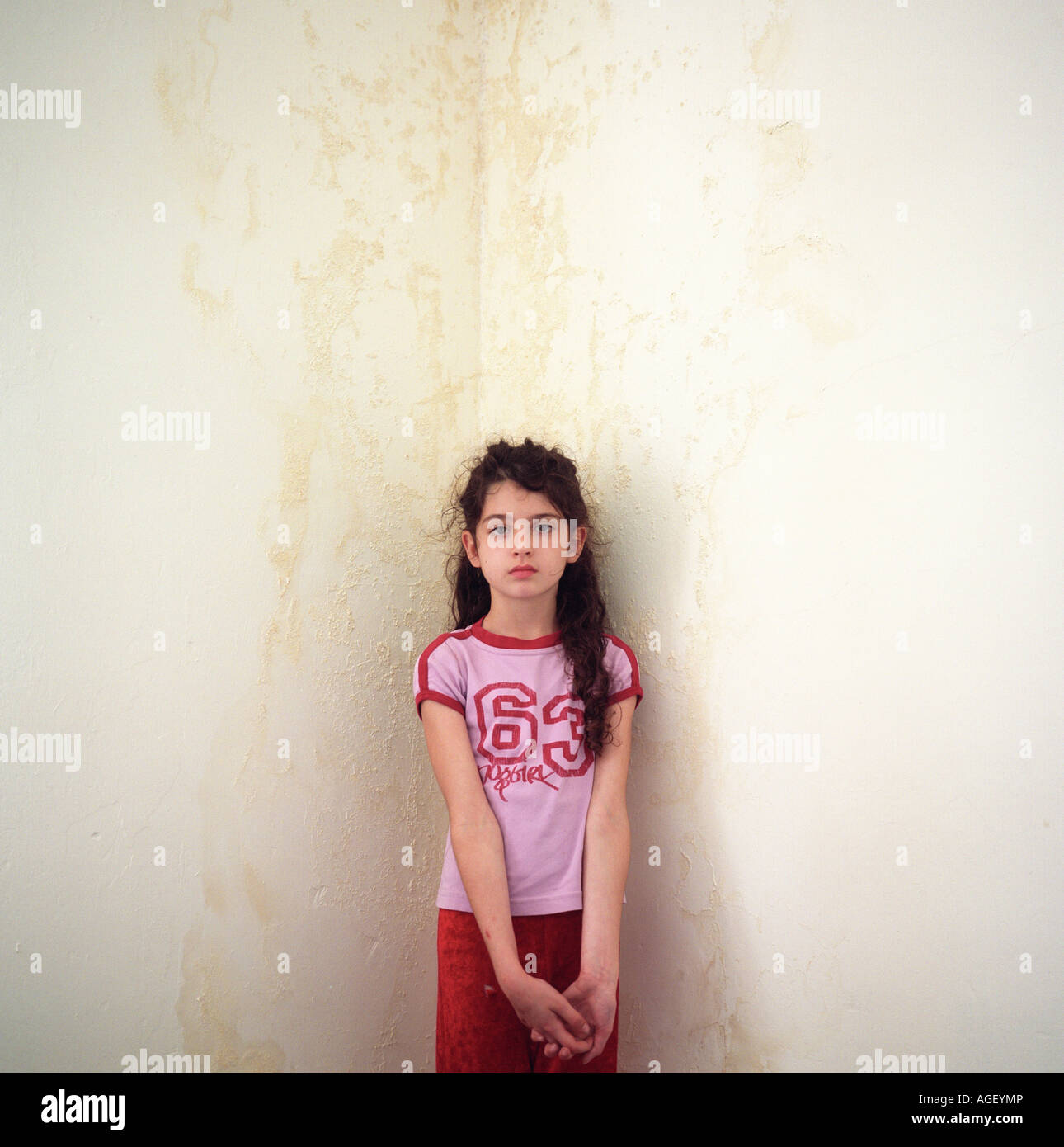 Una ragazza di età compresa tra i 9 in piedi di fronte a una camera da letto a parete ad angolo rovinato dalla presenza di umidità. Foto Stock
